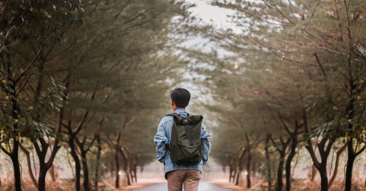 Persona caminando por un sendero pavimentado con mochila y ropa cómoda en un día soleado